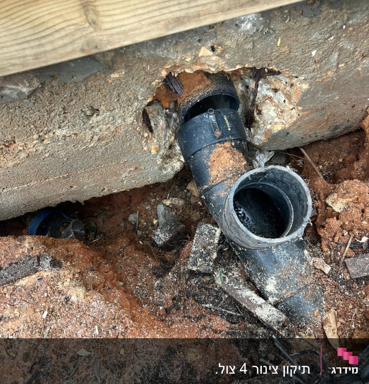 צינור שחור שבור בקיר בטון עם אדמה מסביב